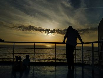 Rear view of man standing on boat deck against sky during sunset
