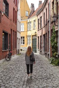 Rear view of woman walking on alley amidst buildings