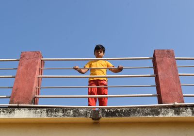 Boy standing on railing against clear sky