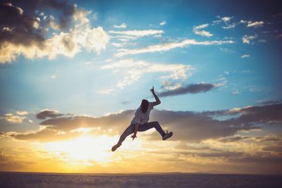 Man jumping over salt flat against sky during sunset