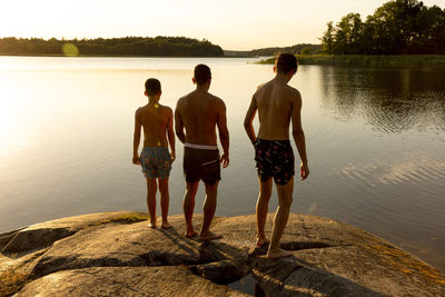 Rear view of father with sons standing on rock at sunset during vacation