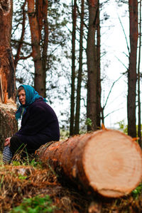 Russian grandmother senior old woman seating on log in pine autumn forest. old women in coat 