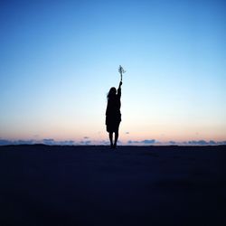 Silhouette woman holding plant while standing on field against sky during sunset