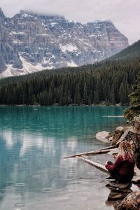 Woman sitting by lake against mountains