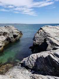 Rocks on shore by sea against sky