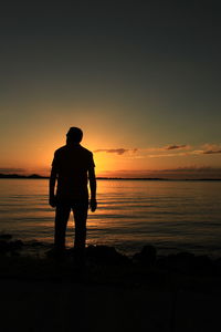 Rear view of silhouette man on beach against sky during sunset