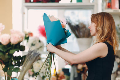 Side view of woman holding flower bouquet while standing at home