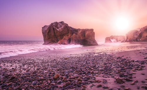 Rocks on beach against sky during sunset