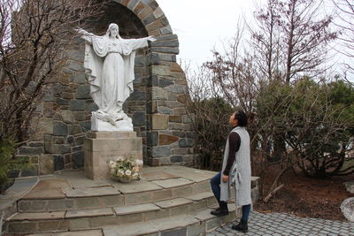 Woman standing by statue against bare trees