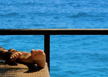 Low section of woman relaxing on seat against sea