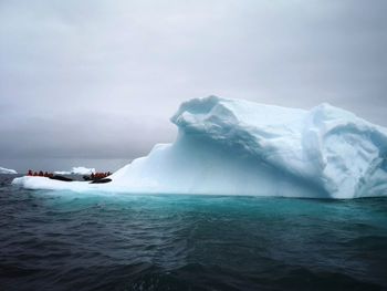 Scenic view of iceberg and people on boats watching seals in antarctica.