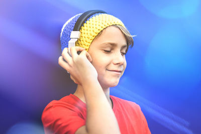 Portrait of a smiling beautiful boy listening music with headphones isolated on a blue background. 