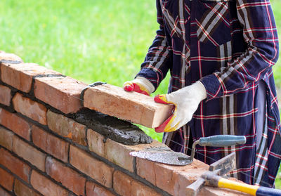 Young woman builds a wall of bricks, lays bricks on cement-sand mortar