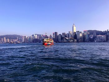 Nautical vessel on sea by buildings against clear sky in city