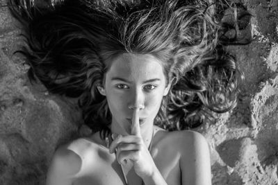 Directly above portrait of teenage girl lying down at beach with finger on lips