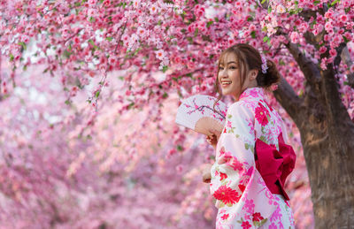 Woman standing by pink cherry blossom