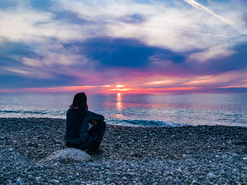 Woman sitting on beach against sky during sunset