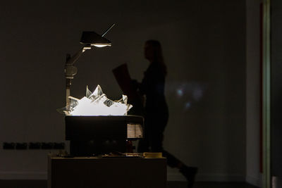 Silhouette man and woman standing by illuminated light on table