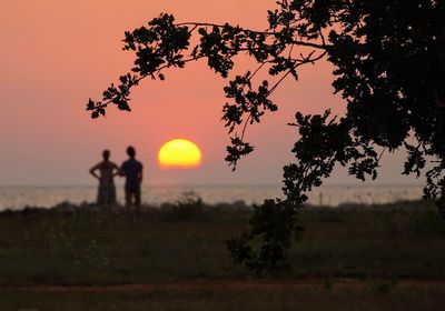 Silhouette people standing on field against sky during sunset