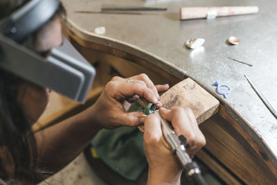 High angle view of female artisan shaping ring with equipment on table in workshop