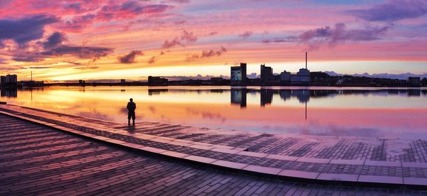 Silhouette man standing by lake against sky during sunset