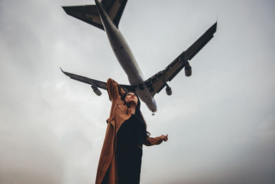 Low angle view of man holding airplane against sky