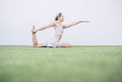 Woman exercising while sitting on grass against sky