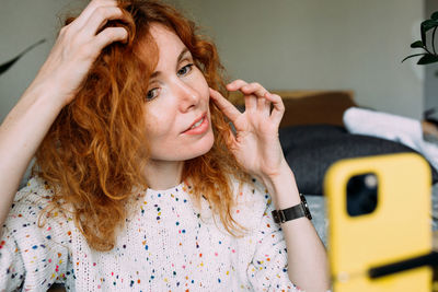 Young curly redhead female blogger filming daily tutorial for social media