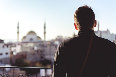 Rear view of man looking at mosque in city against sky