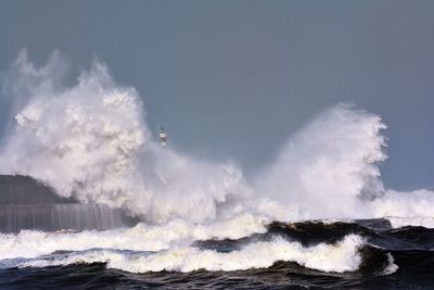 Panoramic view of waves splashing on rocks against sky