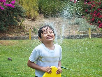 Playful boy enjoying water sprinkling in garden
