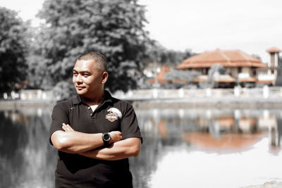 Man with arms crossed standing against lake