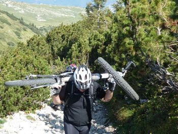 Man with bicycle walking on mountain against trees