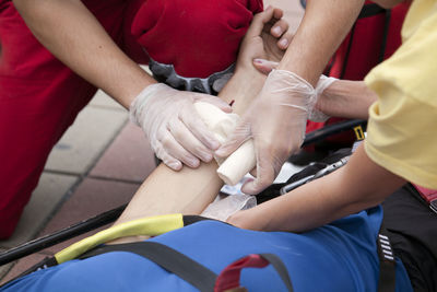 Cropped hands of people bandaging man indoors