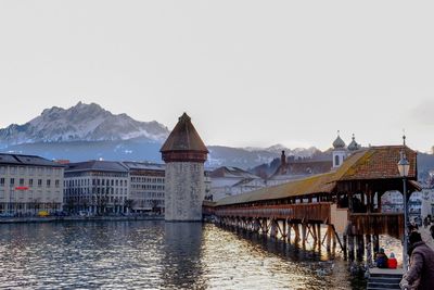 Bridge over river by buildings against clear sky