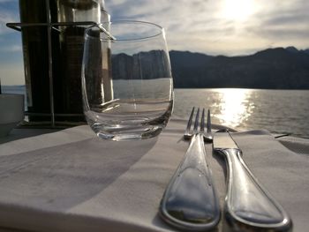 Close-up of fork and knife by glass on table against river during sunny day