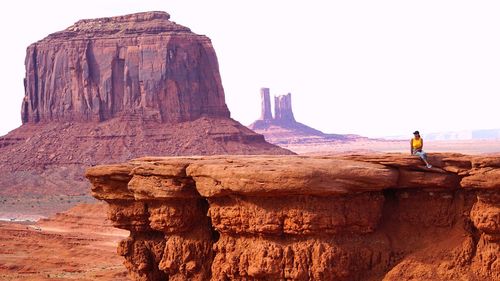 Full length of woman sitting on cliff against sky