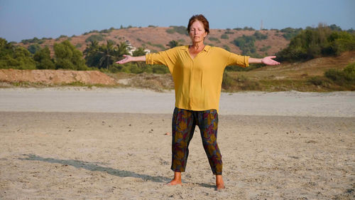Full length of woman with arms outstretched while standing on sand at beach