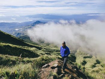 Rear view of man standing on mountain against sky.