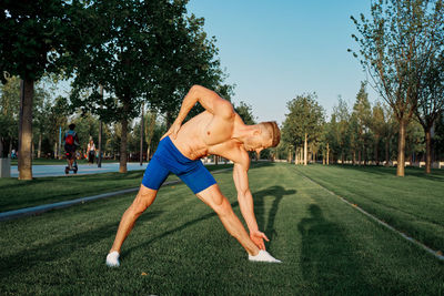 Full length of shirtless man with arms outstretched against trees