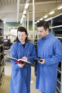 Mid adult female electrician discussing over documents with colleague in industry