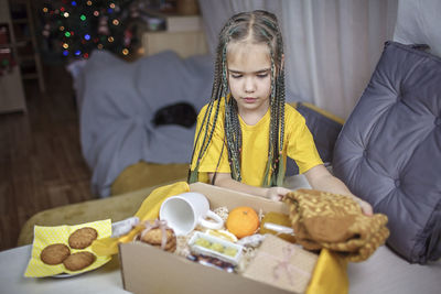 Girl packing care box with tea, honey, cookies and knitted wool socks for grandmother on christmas