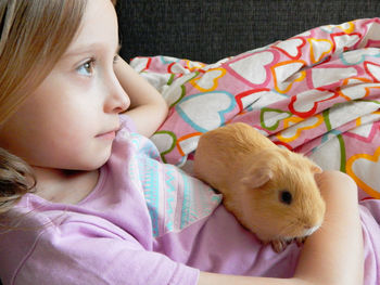 Close-up of cute girl with guinea pig relaxing on bed at home