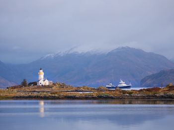 Lighthouse amidst buildings and mountains against sky