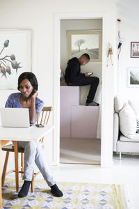 Mid adult woman using laptop at table with son sitting in storage room