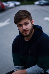 Portrait of young man wearing hooded shirt while crouching on road