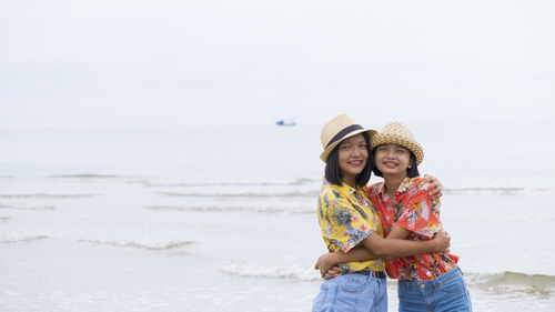 Portrait of cute friends embracing while standing against sea