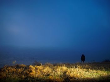 Rear view of silhouette man walking on field against clear sky
