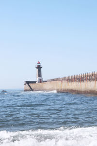 Lighthouse by sea against clear sky