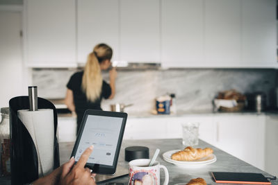 Cropped hand of woman holding digital tablet against teenage girl adjusting home automation in kitchen